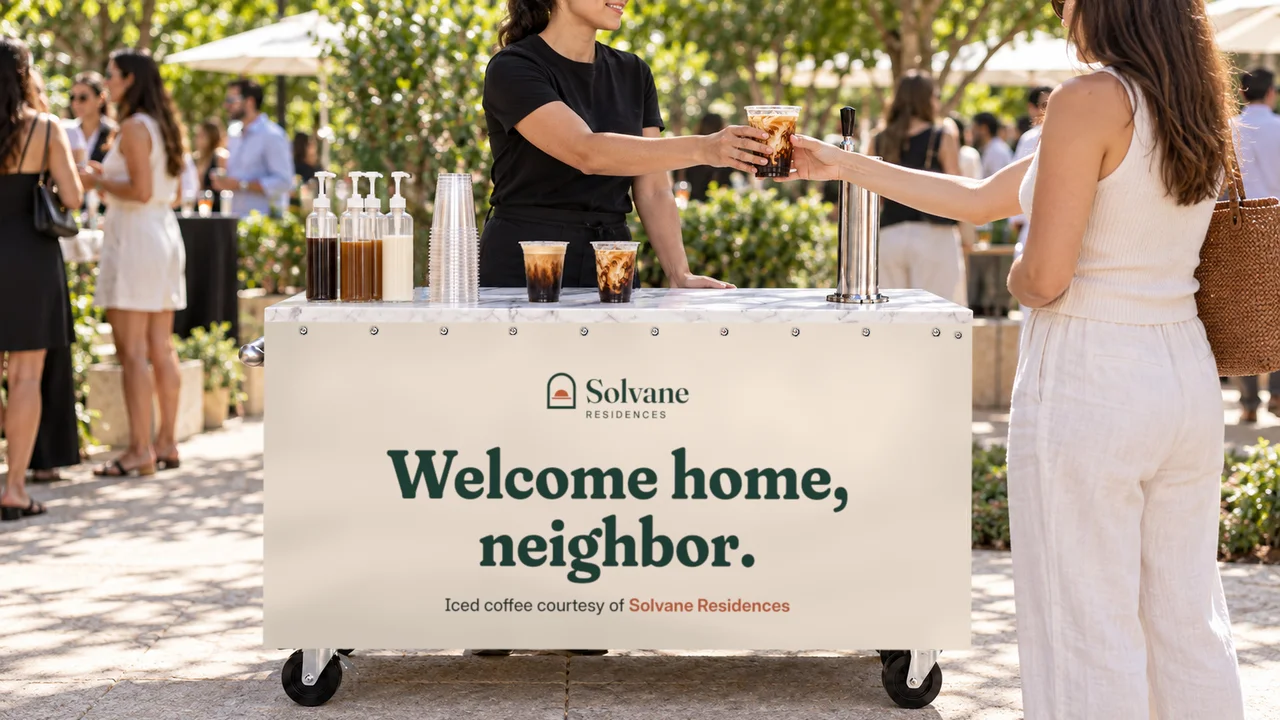 A barista hands an iced coffee to a guest at a cart branded "Welcome home, neighbor"